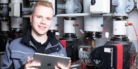 Ein junger Anlagenmechaniker vor einer Heizungsanlage, der ein Tablet hält
