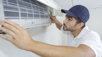 Ein Mechatroniker installiert eine Klimaanlage an der Wand und trägt eine Schirmmütze auf dem Kopf.